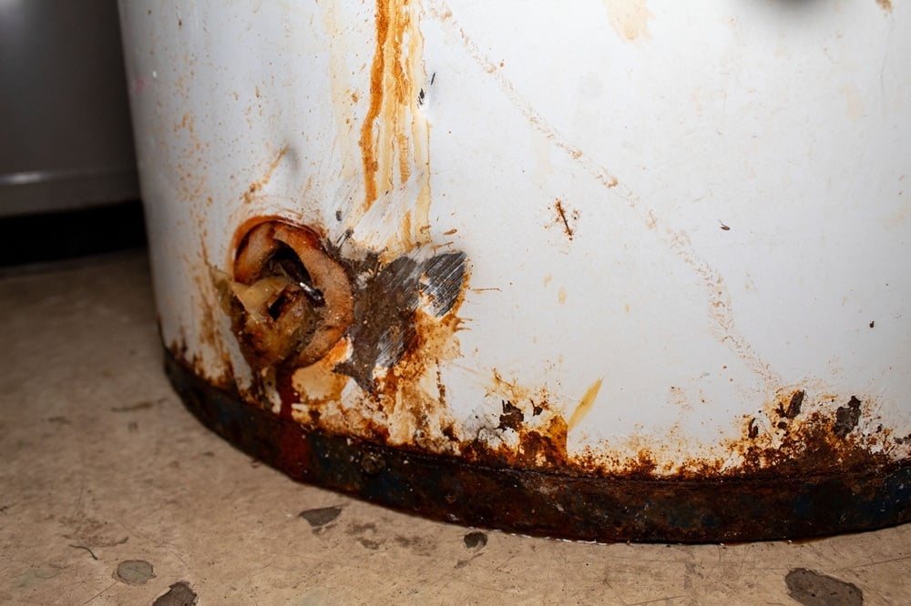 Severely rusted water heater tank with bottom corrosion and active leak, showing failure caused by long term internal tank rust